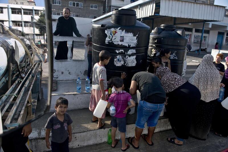 Palestinians, displaced by violence and living at a UN school in Gaza City, fill up their plastic jugs as a water supply truck makes its daily delivery (AFP PHOTO/ROBERTO SCHMIDT)