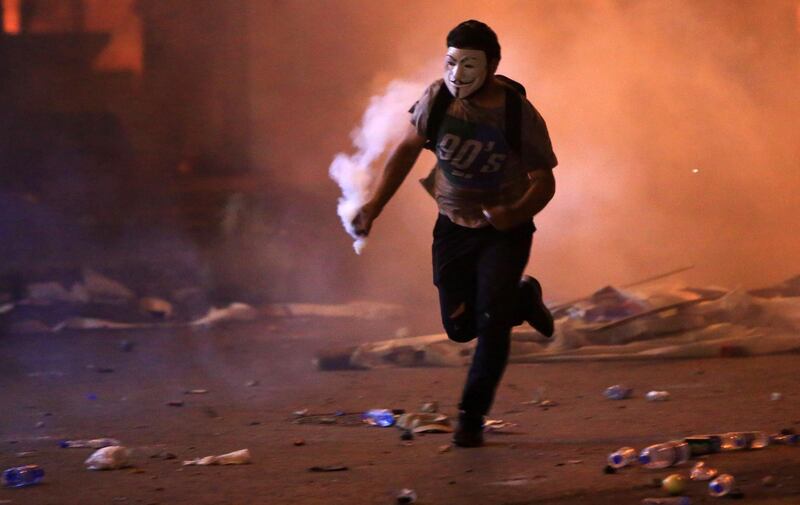 A masked Lebanese demonstrator runs with a tear gas canister amid clashes with security forces during a mass protest at Riad al-Solh Square in the centre of the capital Beirut. AFP