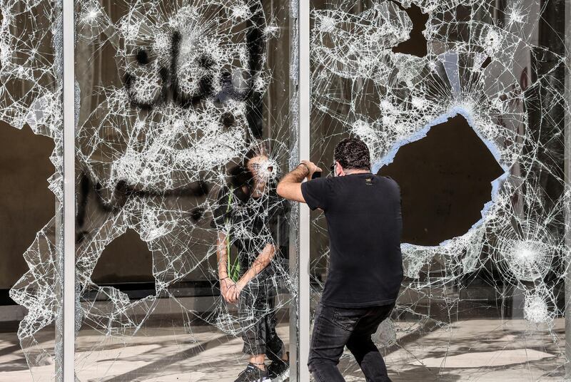 A protester poses for a photo behind smashed glass and slogan reading in Arabic 'Lebanon only' during students protest in Beirut on November 12, 2019.  EPA