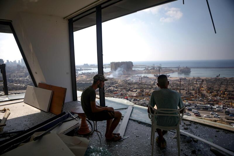 Two men gaze at the devastated Beirut port from a damaged building in the nearby neighbourhood of Mar Mikaehl on August 6, 2020, two days after a massive blast there shook the Lebanese capital.  The huge blast at Beirut port has killed at least 137 people, left dozens missing and at least 5,000 wounded, a Lebanese health ministry spokesperson said today. / AFP / Patrick BAZ
