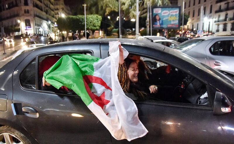 An Algerian holds a national flag while sitting out the window of a car during a demonstration in the centre of the capital Algiers on March 11, 2019, after President Abdelaziz Bouteflika announced his withdrawal from a bid to win another term in office and postponed an April 18 election, following weeks of protests against his candidacy.  Bouteflika, in a message carried by national news agency APS, said the presidential poll would follow a national conference on political and constitutional reform to be drawn up by the end of 2019. / AFP / RYAD KRAMDI                         
