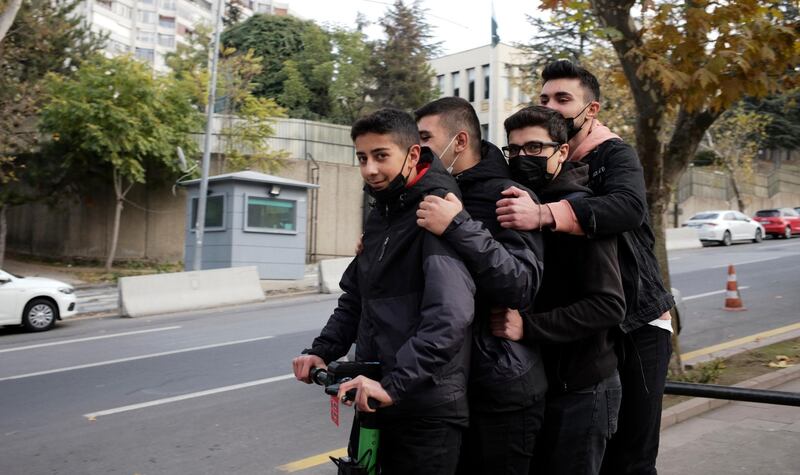 Four youngster riding on one scooter roll down a popular street, in Ankara, Turkey. Turkey is re-introducing a series of restrictions, including partial weekend lockdowns. AP Photo