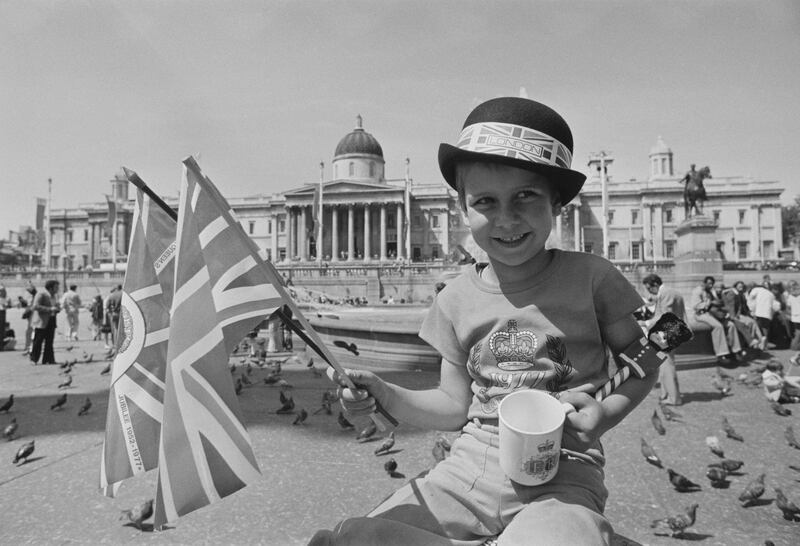 A young boy holding two British flags and a cup with the jubilee logo, celebrates the silver jubilee in Trafalgar Square, central London in June 1977. 
