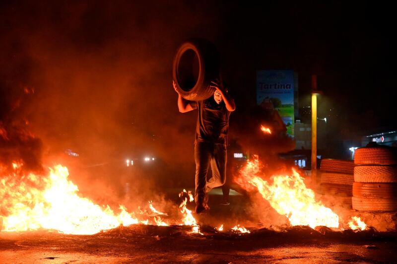 A protester throws a tyre on a fire lit by protesters to block the Dora highway in Beirut.  EPA