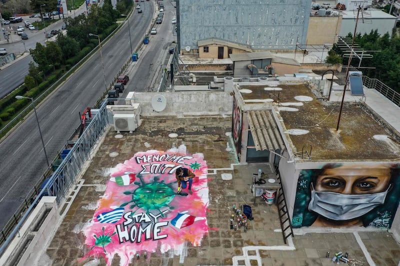 This picture taken on March 23, 2020 shows artist S.F., 16, spraypainting graffiti inspired by the COVID-19 novel coronavirus on the roof of his apartment building in Athens.  - RESTRICTED TO EDITORIAL USE - MANDATORY MENTION OF THE ARTIST UPON PUBLICATION - TO ILLUSTRATE THE EVENT AS SPECIFIED IN THE CAPTION
 / AFP / Aris Messinis / RESTRICTED TO EDITORIAL USE - MANDATORY MENTION OF THE ARTIST UPON PUBLICATION - TO ILLUSTRATE THE EVENT AS SPECIFIED IN THE CAPTION
