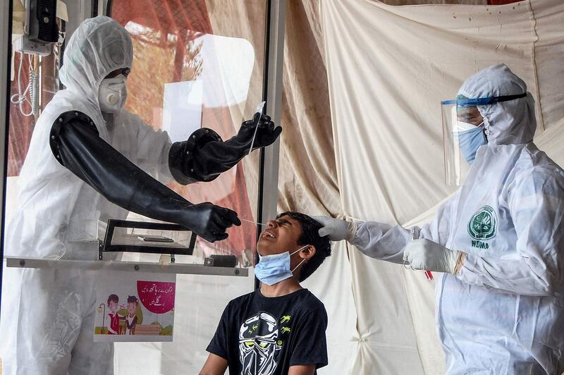 Health officials wearing protective gear take a nasal swab sample from a young boy at a testing facility in Hyderabad, Pakistan. AFP