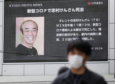 A man wearing a protective face mask, following an outbreak of the coronavirus disease (COVID-19), walks past in front of a huge screen reporting death of Japanese comedian Ken Shimura, who had been hospitalised after being infected with the new coronavirus, in Osaka, western Japan March 30, 2020, in this photo taken by Kyodo. Mandatory credit Kyodo/via REUTERS ATTENTION EDITORS - THIS IMAGE WAS PROVIDED BY A THIRD PARTY. MANDATORY CREDIT. JAPAN OUT. NO COMMERCIAL OR EDITORIAL SALES IN JAPAN.