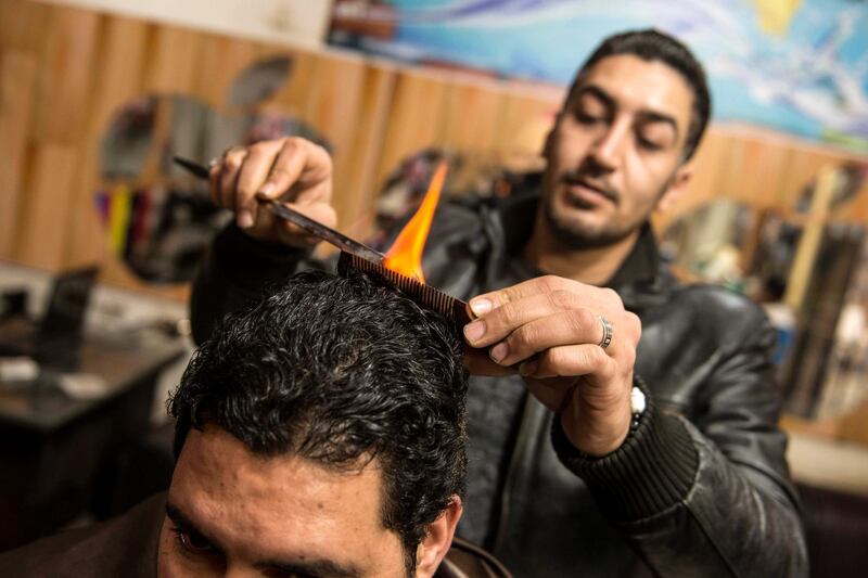 Egyptian barber Hamada Ramadan uses fire to straighten the hair of a customer at his shop in Faisal District, Giza, Egypt.  EPA
