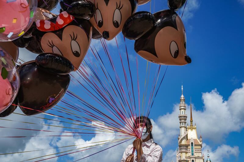 An employee wearing a protective mask holds Mickey and Minnie Mouse shaped balloons at Walt Disney Co.'s Disneyland Resort in Hong Kong, China. Bloomberg