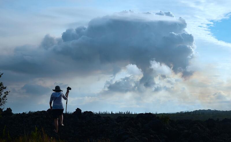 A man climbs onto a petrified lava flow from long ago for a picture of the plume of volcanic smoke in the distance over the area of Leilani Estates near the town of Pahoa. Frederic Brown / AFP