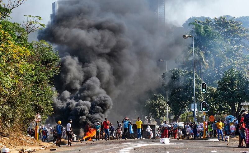 A crowd watches smoke billowing into the sky alongside a burning barricade in Durban. Mr Ramaphosa says there is no justification for violence and that it is damaging efforts to rebuild the economy.