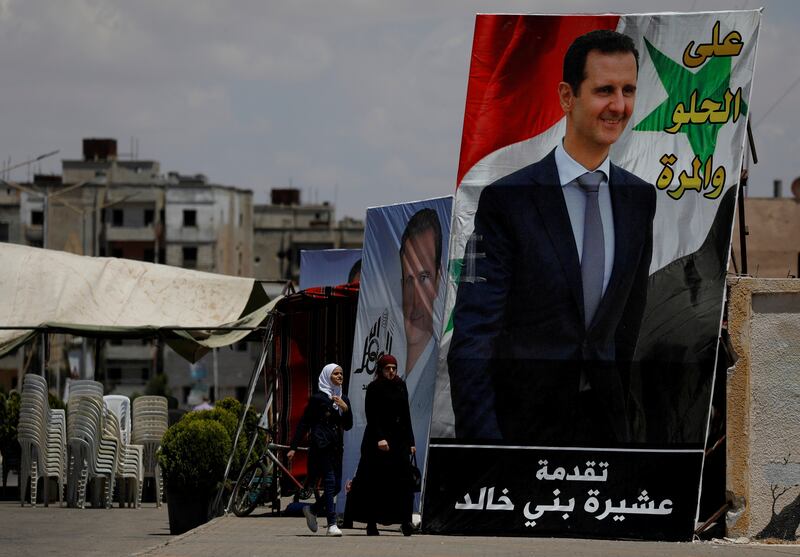 People walk past posters depicting Syria's President Bashar Al Assad.