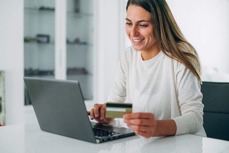 Beautiful smiling young woman holding a credit card and typing on a laptop at home. Getty Images