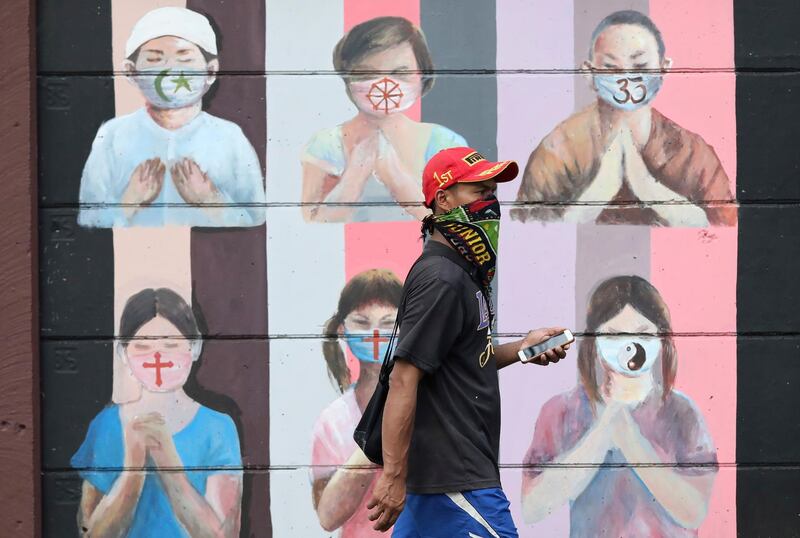 A man wearing a face mask walks past a coronavirus awareness mural depicting children of various faiths praying while wearing face masks in Depok, Indonesia, AP