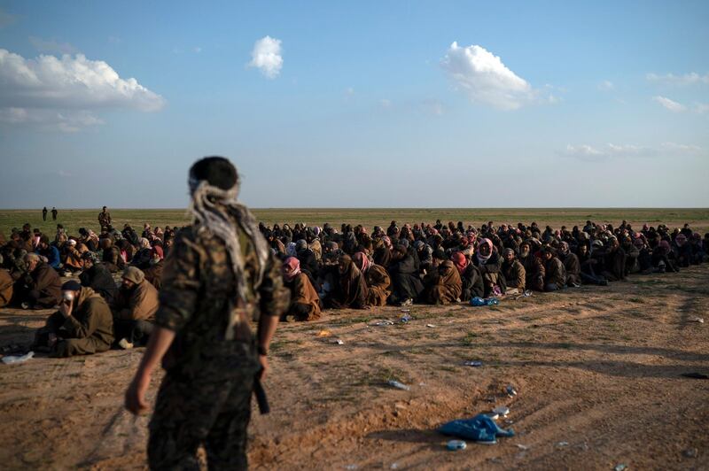 FILE - In this Feb. 22, 2019 file photo, U.S.-backed Syrian Democratic Forces (SDF) fighters stand guard next to men waiting to be screened after being evacuated out of the last territory held by Islamic State group militants, near Baghouz, eastern Syria. The SDF fighters who drove the Islamic State from its last strongholds called Monday, March 25, 2019, for an international tribunal to prosecute hundreds of foreigners rounded up in the nearly five-year campaign against the extremist group. (AP Photo/Felipe Dana, File)