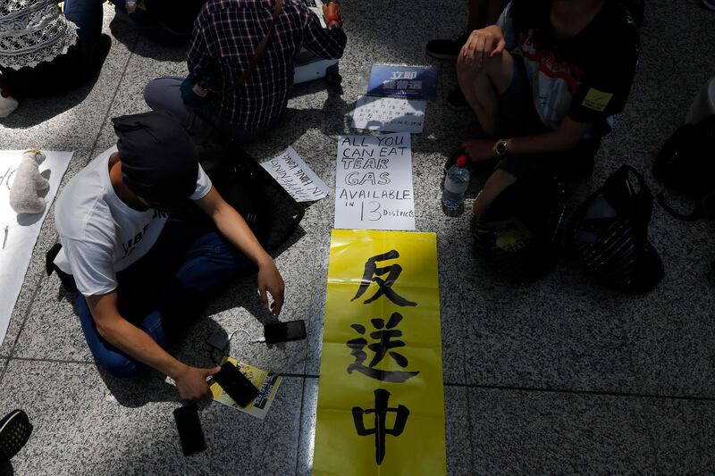 Demonstrators sit down with banners which reads "Anti extradition to China" "All you can eat Tear Gas in 13 districts" at the airport. AP Photo