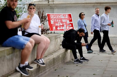 Pedestrians walk past a sign covered in stickers from an anti-vaccine demonstration, asking people to social distance, near Marble Arch in central London on June 6, 2021. The Delta variant of the coronavirus, first discovered in India, is estimated to be 40 percent more transmissible than the Alpha variant that caused the last wave of infections in the UK, Britain's health minister said Sunday. / AFP / Tolga Akmen
