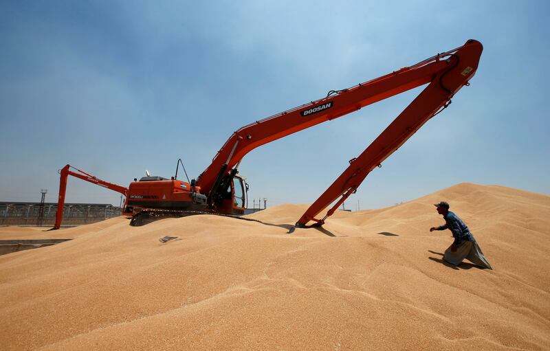 A worker helps an excavator to collect wheat grain at a silo in Mosul, Iraq. Reuters