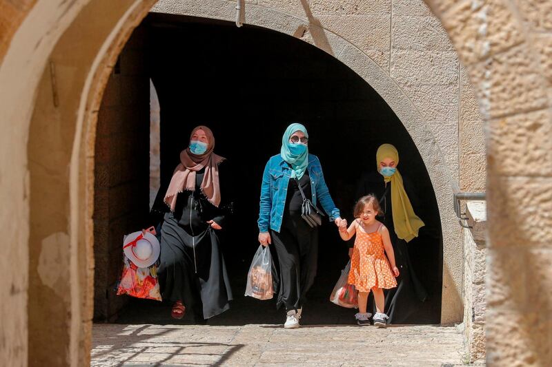 Palestinian women and children wearing masks walk in an alley in the Old City of Jerusalem.  AFP