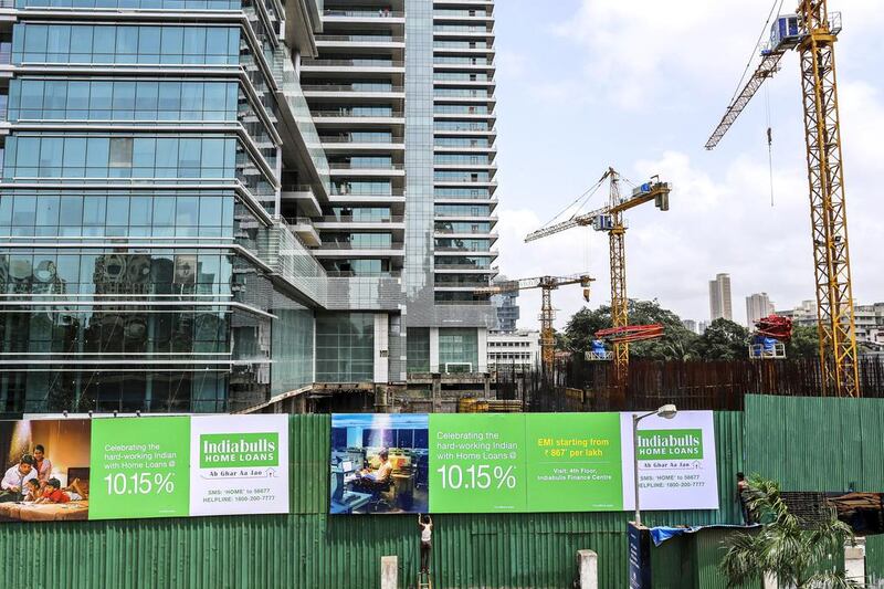 A labourer fixes a billboard, displaying a Indiabulls Real Estate home loan advertisement, to the boundary wall of a construction site in the Lower Parel area of Mumbai. Dhiraj Singh / Bloomberg