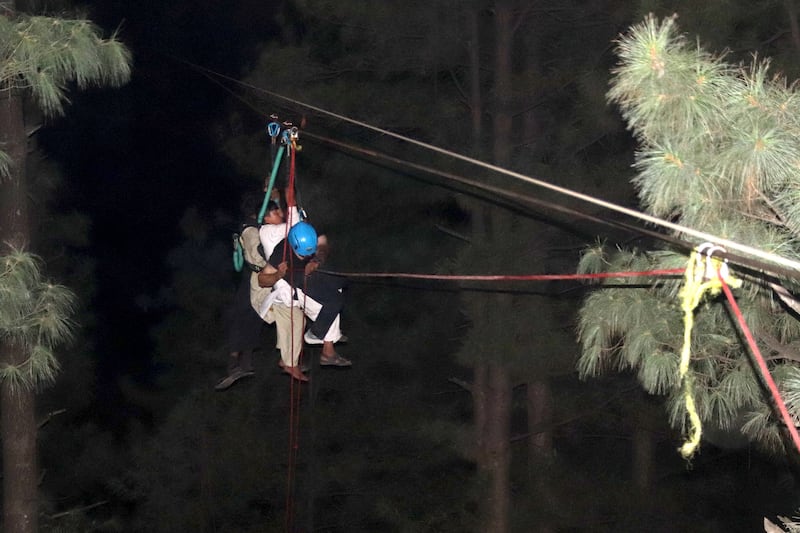 A Pakistani soldier carries a young person from the broken cable car to safety using a zipline. EPA