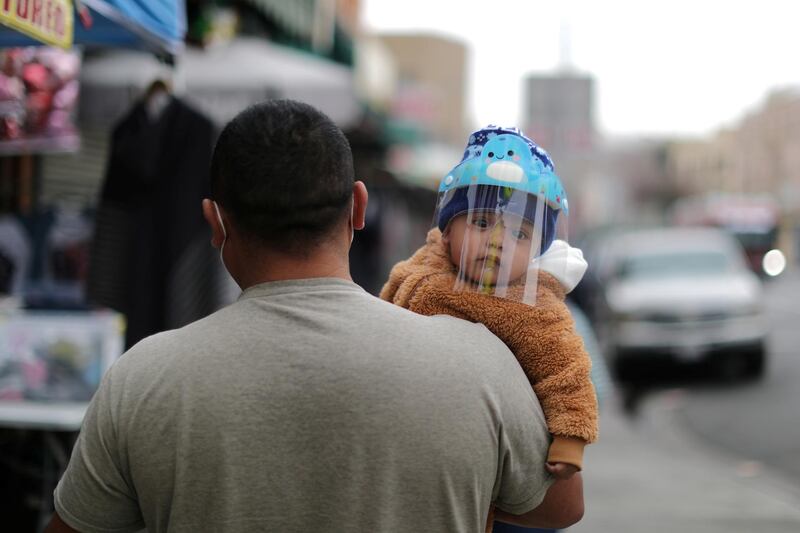 A Los Angeles man carries a baby wearing a face shield to protect him against Covid-19. Reuters