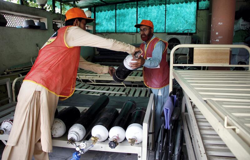 Aziz Ullah, 60, and 21-year-old Muhammad Usman, both aid workers of Alamgir Welfare Trust are arranging oxygen cylinders at the warehouse of the non-profit organization in Islamabad, the capital city of Pakistan. Imran Mukhtar/ The National 