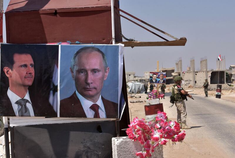 Members of Russian and Syrian forces stand guard near posters of Syrian President Bashar al-Assad and his Russian counterpart Vladimir Putin at the Abu Duhur crossing on the eastern edge of Idlib province on August 20, 2018. - Civilians are coming from rebel-held areas in Idlib province and entering regime-held territories through the Abu Duhur crossing, some of them returning to their villages that were recaptured by the regime forces earlier this year. (Photo by George OURFALIAN / AFP)