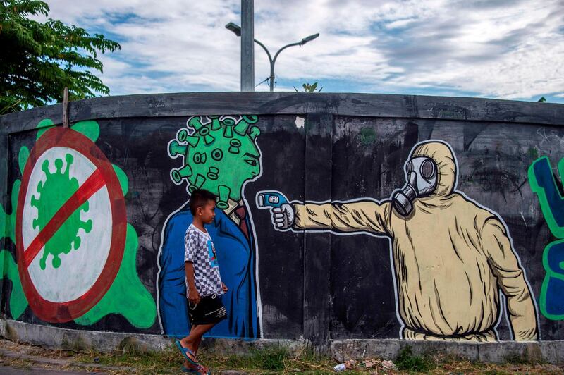 A boy walks past a mural depicting the Covid-19 coronavirus in Surabaya, East Java. AFP