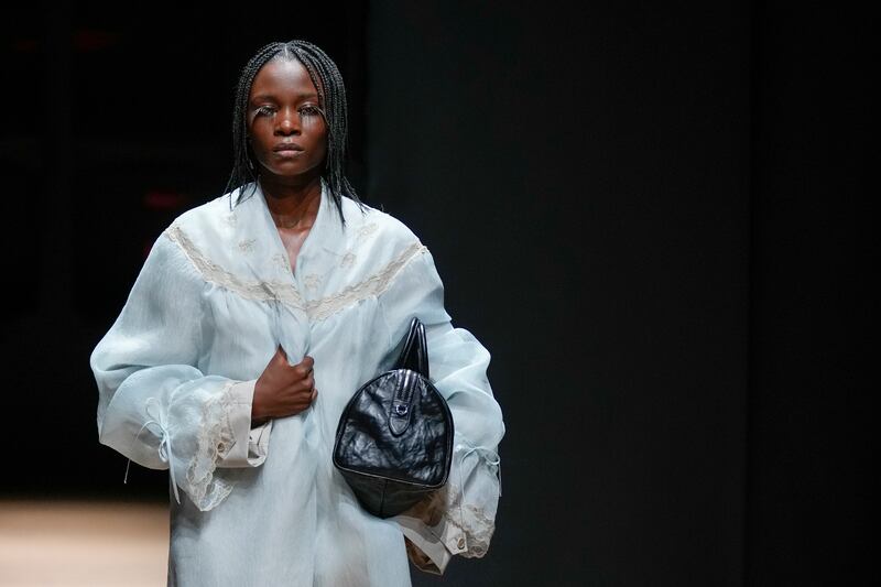 A model with long feathery eyelashes clutches a lace trimmed house coat on the Prada runway. AP