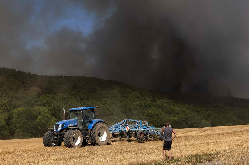 A farmer stands in a field as farmers arrive with their tractors to help firefighters to fight a nearby forest fire in Thierville, in Normandy, north-western France. AFP