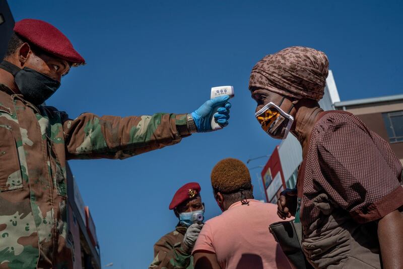 FILE - In this file photo taken Wednesday May 20, 2020, South African National Defense Forces check the temperature  of people near the Pan Africa taxi rank in Johannesburg's Alexandra township. South Africa is struggling to balance its fight against the coronavirus with its dire need to resume economic activity. The country with the Africaâ€™s most developed economy also has its highest number of infections â€” more than 19,000. (AP Photo/Jerome Delay, File)