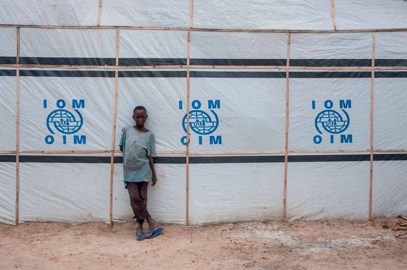 A boy stands against a temporary structure erected by the IOM (International Organization for Migration) in Pulka on August 1, 2018. - As the presidential race heats up ahead of February polls, the Nigerian government and officials of Borno state, the epicentre of the Boko Haram Islamist insurgency, are encouraging and facilitating the "return" of tens of thousands of people. As he campaigns for a second term in office, the incumbent president is working to show that he has delivered on his pledge to defeat the Islamists. But the reality is that people are being sent back to camps across Borno state while Boko Haram is still launching devastating attacks against military and civilian targets. Pulka is a garrison town built on a model becoming increasingly common across Nigeria's remote northeast region: a devastated town turned into a military base so soldiers can protect satellite camps and humanitarian agencies can distribute aid. (Photo by Stefan HEUNIS / AFP)