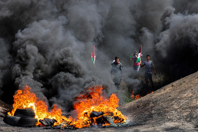 Men with Palestinian flags walk through the fumes from flaming tires during a demonstration along the border with Israel east of Gaza City on April 5, 2023.  - Israeli police said they had entered to dislodge "agitators" from Jerusalem's al-Aqsa Mosque, a move denounced as an "unprecedented crime" by the Palestinian Islamist movement Hamas.  The holy Muslim site is built on top of what Jews call the Temple Mount, Judaism's holiest site.  (Photo by MAHMUD HAMS  /  AFP)