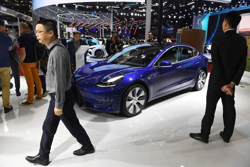 Visitors walk past a Tesla Model 3 at the Shanghai Auto Show in Shanghai on April 17, 2019.   / AFP / GREG BAKER
