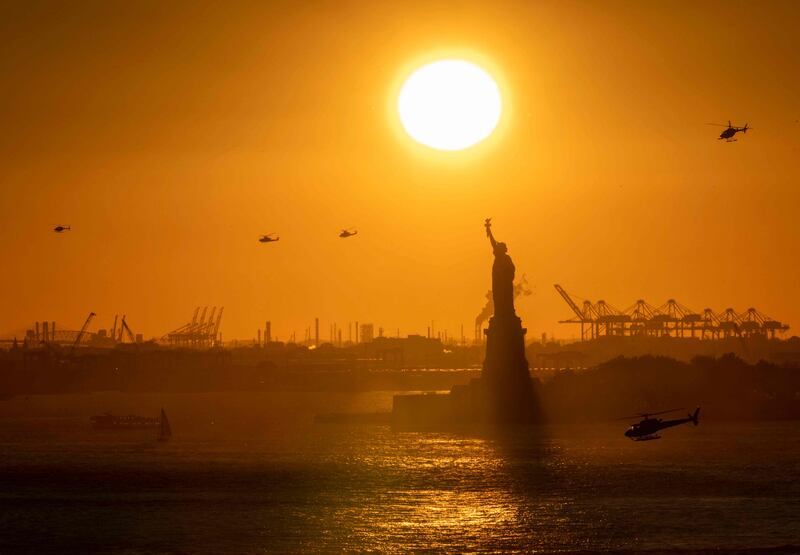 Helicopters fly in the distance as the sun sets behind the Statue of Liberty in New York Harbour. AFP
