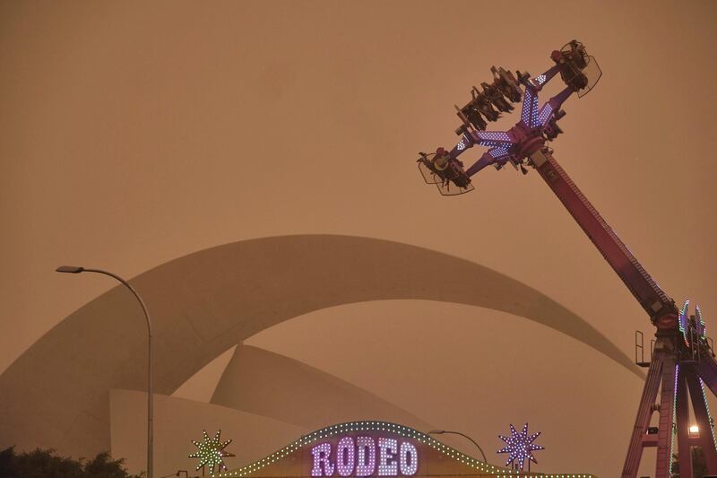 People ride on a fairground attraction in a cloud of red dust in Santa Cruz de Tenerife, Spain. AP Photo