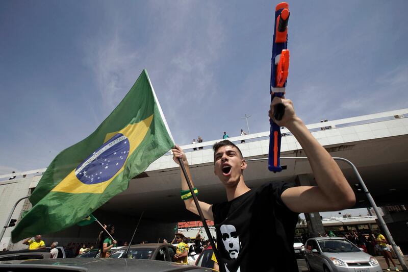 A demonstrator holds a toy gun and a Brazilian flag, during a race in support of Jair Bolsonaro, presidential candidate for the National Social Liberal Party, in the center of Brasilia, Brazil, Saturday, Oct. 6, 2018. Brazil will hold general elections on Oct. 7. (AP Photo/Eraldo Peres)