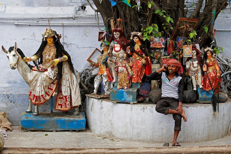 A labourer speaks on his mobile phone as he takes rest in front of idols of Hindu deities which are kept under a tree at a market area in Kolkata, India, April 2, 2018. REUTERS/Rupak De Chowdhuri