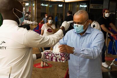 In this Sunday, April 19, 2020 photo, a security guard checks a customer's temperature and offers him disposable gloves amid the coronavirus pandemic in the world's busiest Carrefour supermarket at the Mall of the Emirates in Dubai, United Arab Emirates. One of the biggest private employers in the Middle East hasn't yet cut salaries or laid off any of its 44,000 workers, but the pandemic is changing how Majid Al Futtaim, the company that owns and operates hundreds of grocery stores and more than two dozen malls, thinks about food security, retail and tourism. (AP Photo/Jon Gambrell)