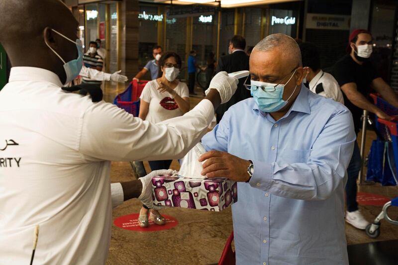 In this Sunday, April 19, 2020 photo, a security guard checks a customer's temperature and offers him disposable gloves amid the coronavirus pandemic in the world's busiest Carrefour supermarket at the Mall of the Emirates in Dubai, United Arab Emirates. One of the biggest private employers in the Middle East hasn't yet cut salaries or laid off any of its 44,000 workers, but the pandemic is changing how Majid Al Futtaim, the company that owns and operates hundreds of grocery stores and more than two dozen malls, thinks about food security, retail and tourism. (AP Photo/Jon Gambrell)