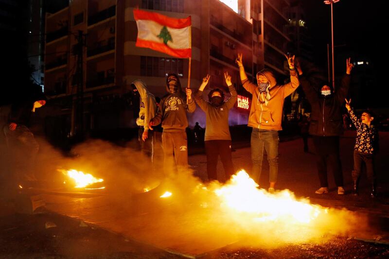 Anti-government demonstrators hold a national flag as burning tires block a road during a protest in Beirut, Lebanon, Thursday, Jan. 16, 2020. Lebanese protesters Thursday decried security forces' use of violence during rallies over the past two days, including attacks on journalists and the detention of over 100 people. (AP Photo/Bilal Hussein)