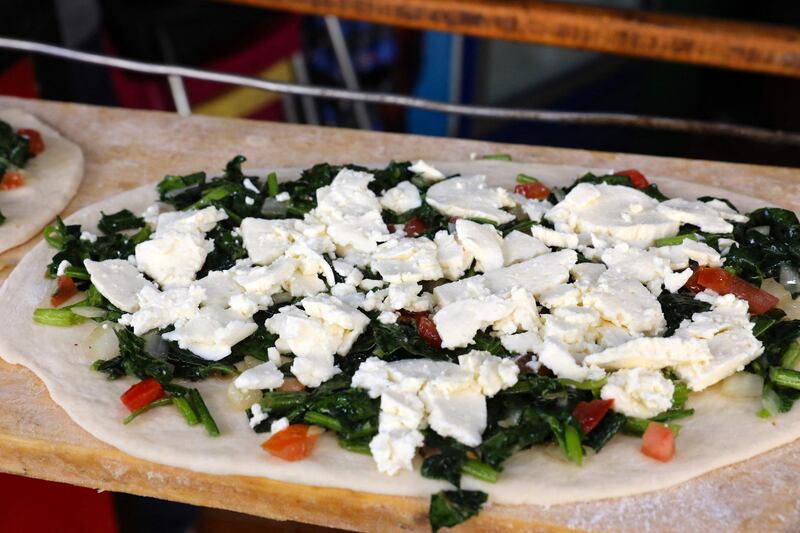 Flattened dough garnished with cheese and leafy vegetables is ready to be baked. AFP