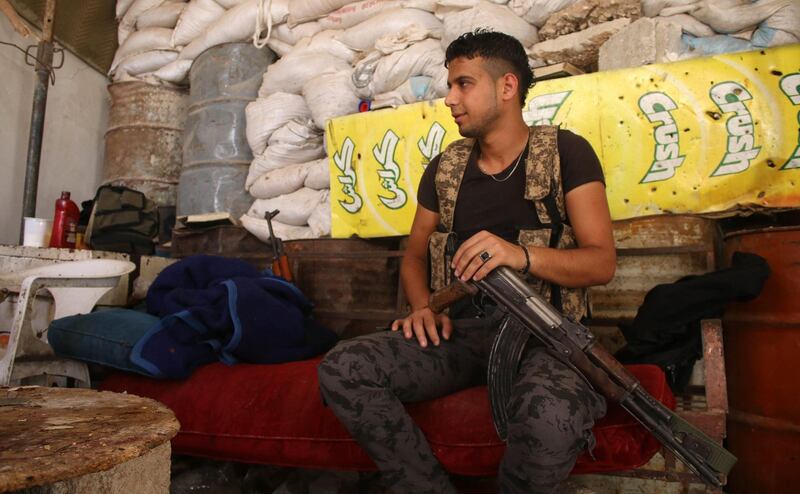 Moawiya Sayasina sits holding a Kalashnikov assault rifle at a position fortified with sandbags near the frontline in a rebel-held neighbourhood in the southern Syrian city of Daraa. Mohamad Abazeed / AFP