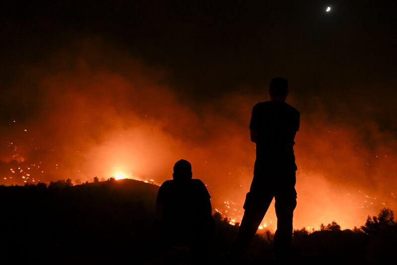 People watch the fires near the village of Malona in the Greek island of Rhodes on July 23, 2023.  Tens of thousands of people fled wildfires on the Greek island of Rhodes on July 23, 2023, as terrified tourists scrambled to get home.  Firefighters tackled blazes that erupted in peak tourism season, sparking the country's largest-ever wildfire evacuation -- and leaving flights and holidays cancelled.  (Photo by SPYROS BAKALIS  /  AFP)