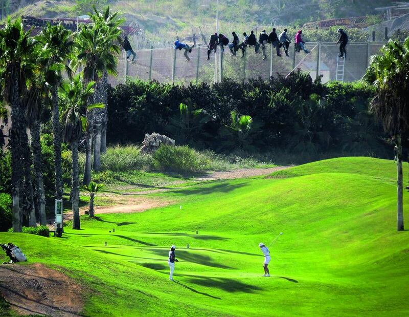 A golfer hits a tee shot as African migrants sit atop a border fence during an attempt to cross into Spanish territory, between Morocco and Spain’s north African enclave of Melilla, in this October 22 file photo. Jose Palazon / Reuters