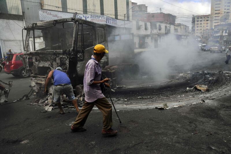 Workers use a crane to move the wreckage of a truck that was burned down during protests in Caracas. AFP