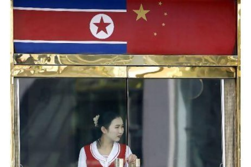 A North Korean waitress stands under the China and North Korean flags at a restaurant in the Chinese border city of Dandong. A reader notes that China is keeping North Korea's antiquated regime in power. AFP / LIU Jin