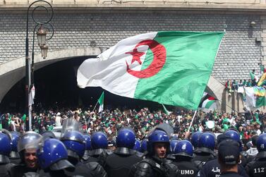 Algerian protesters wave a national flag as security forces stand guard during an an anti-government demonstration in Algiers on April 12, 2019. AFP