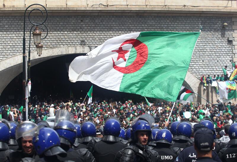 Algerian protesters wave a giant national flag as members of the security forces stand guard during an an anti-government demonstration in the capital Algiers on April 12, 2019.  Algerian protesters gathered for the first Friday protests since the announcement of presidential elections to succeed ousted leader Abdelaziz Bouteflika fearing a ploy by the ruling system to stay in power. / AFP / -
